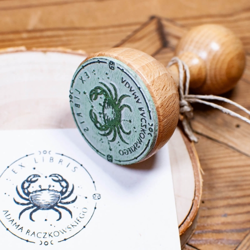 Drewniana pieczątka Ex Libris z grawerem astrologicznego raka – oryginalny prezent dla miłośników znaków zodiaku. Wysokiej jakości guma z precyzyjnym grawerem i klasyczna rączka retro. Produkt personalizowany z imieniem właściciela książki.